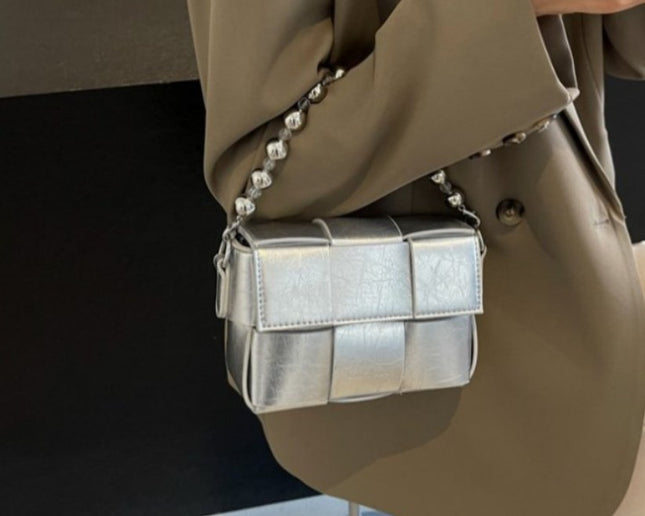 Silver handbag with stylish chain strap. wearing a beige coat against a black background