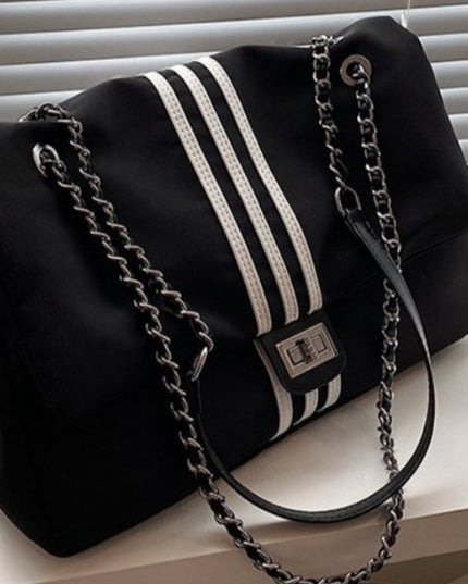 Black stylish handbag with white stripes and a chain strap on a light surface.