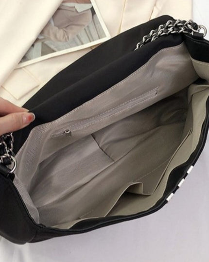 Black stylish handbag with a chain detail held by a person against a neutral background
