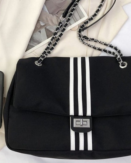 Black stylish handbag with white stripes and a phone on a light-colored fabric background