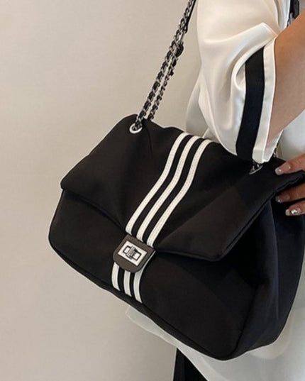 Black stylish handbag with white stripes held by a person wearing a white outfit against a beige background